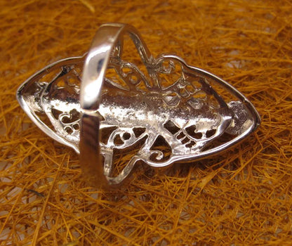 Silver pendant with intricate design on a textured orange surface