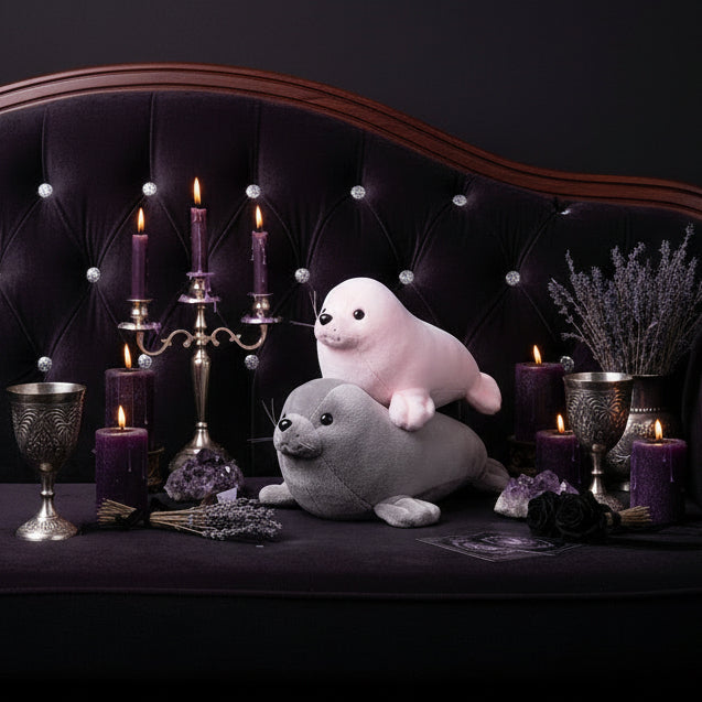 Person holding two plush seals, one pink and one gray, against a blurred indoor background.