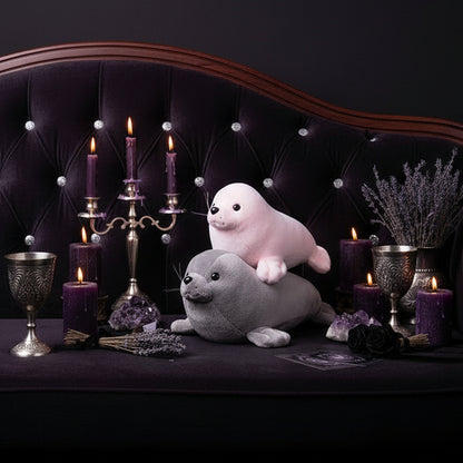 Person holding two plush seals, one pink and one gray, against a blurred indoor background.
