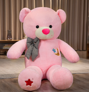 Pink teddy bear with a bow tie on a wooden floor.