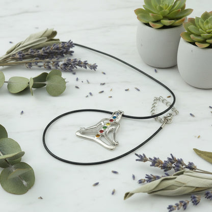 Necklace with a pendant of a person in a meditative pose with colorful stones on a light gray background