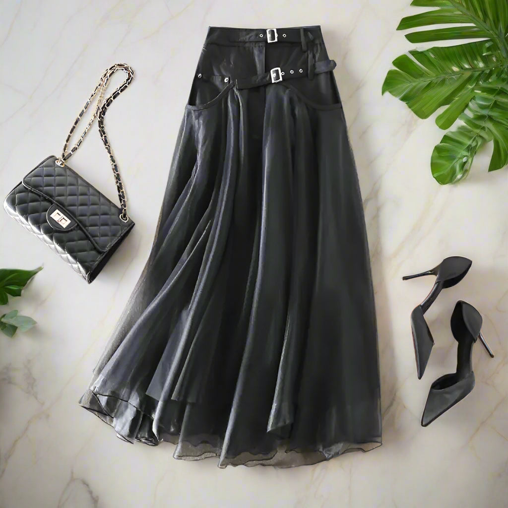 Black skirt with belt, black quilted handbag, and black high heels on a beige background