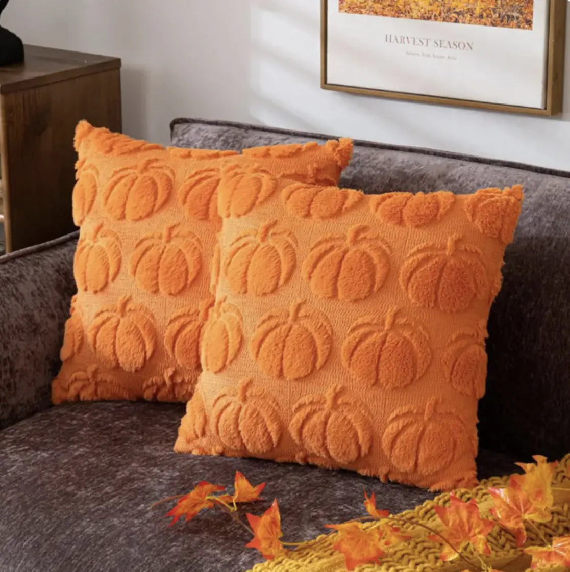Orange textured pillows with pumpkin pattern on a gray sofa.
