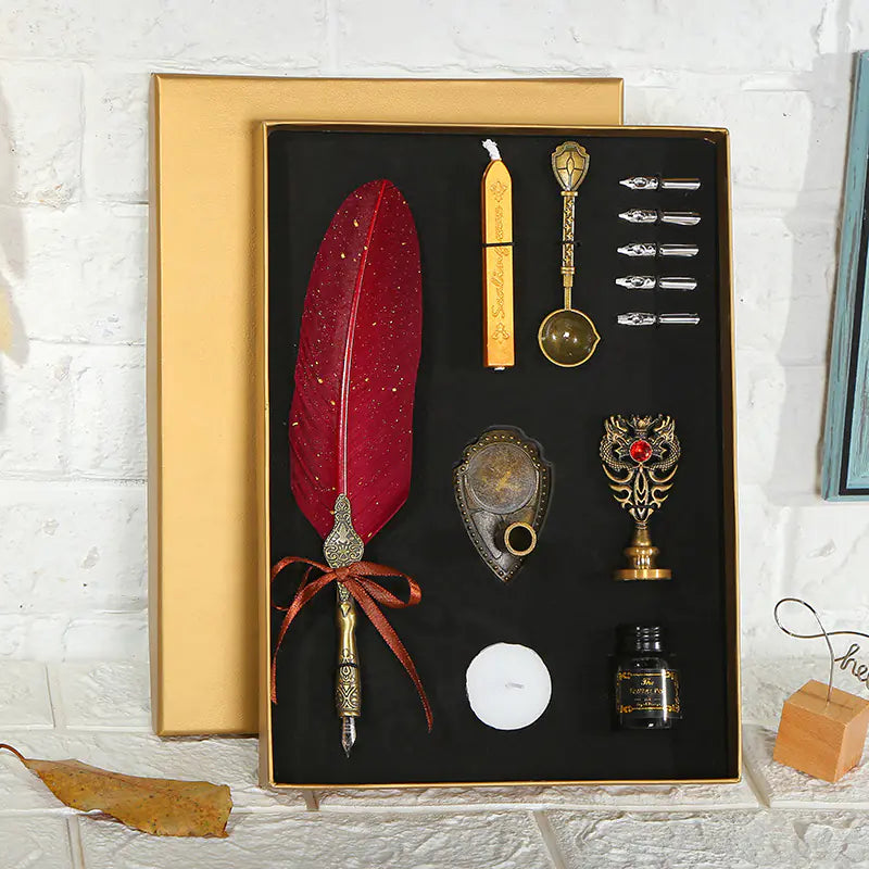 Decorative set with a red feather pen, inkwell, and other accessories in a black box on a white brick wall background.