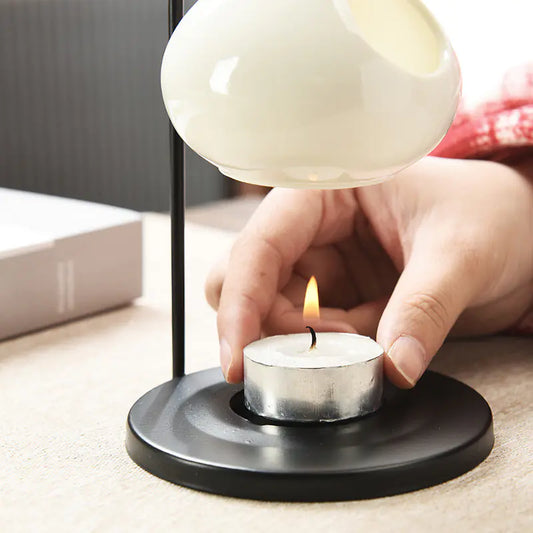 Person lighting a candle under a lampshade on a table.