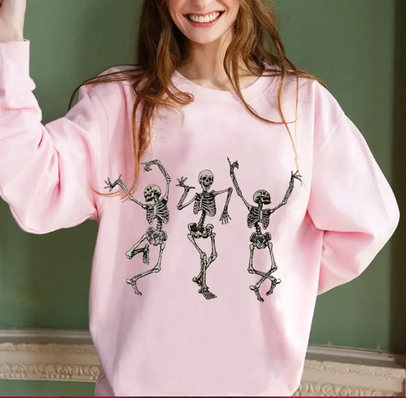 Person wearing a pink sweatshirt with dancing skeletons design against a green wall.