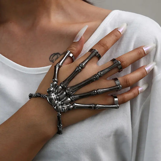 Hand wearing a skeleton hand bracelet on a plain background