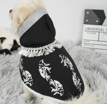 Dog wearing a black hoodie with white patterns on a fluffy surface.