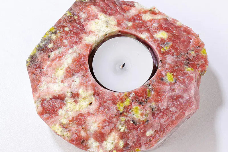 Hexagonal candle holder made of red stone with a white candle inside on a white background