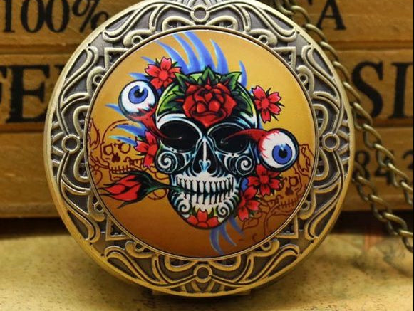 Decorative pocket watch with skull and floral design on a wooden surface
