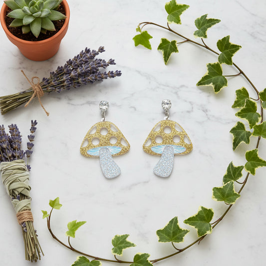 Mushroom-shaped earrings with gold and blue glitter on a white background