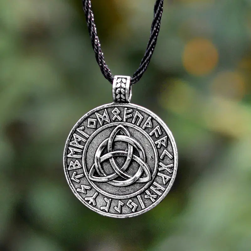 Silver pendant with Celtic knot design and runic text on a blurred green background