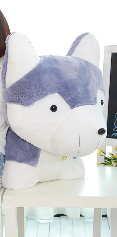 Woman holding a small plush toy and a large plush husky toy in a room.