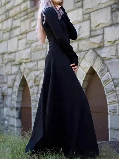 witchy women wearing a long black dress standing in front of a stone wall.