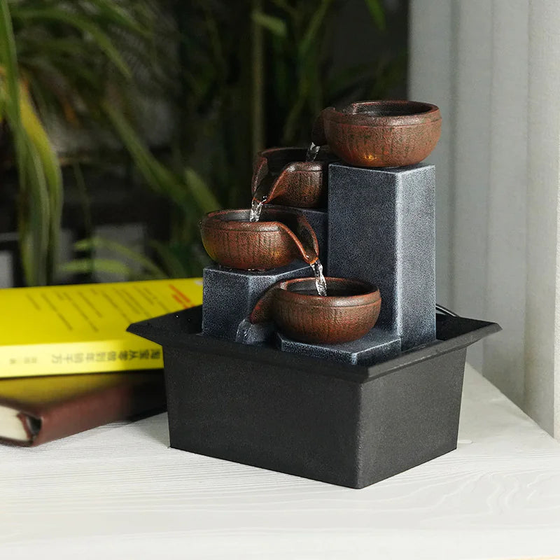 Small black and brown decorative fountain on a surface with books and plants in the background