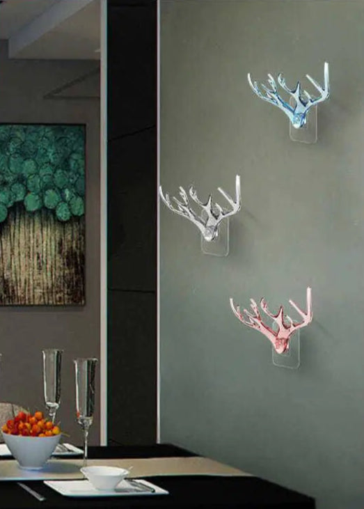 Decorative wall hooks shaped like antlers in different colors on a gray wall.