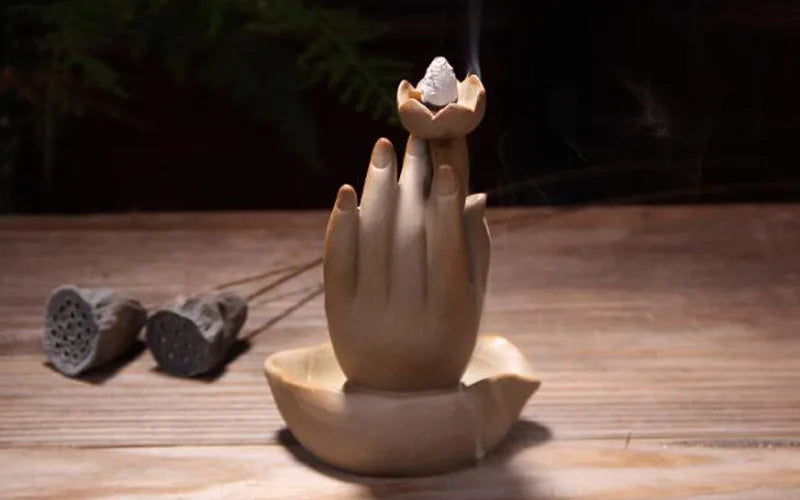 Wooden hand-shaped incense burner with incense on a wooden surface
