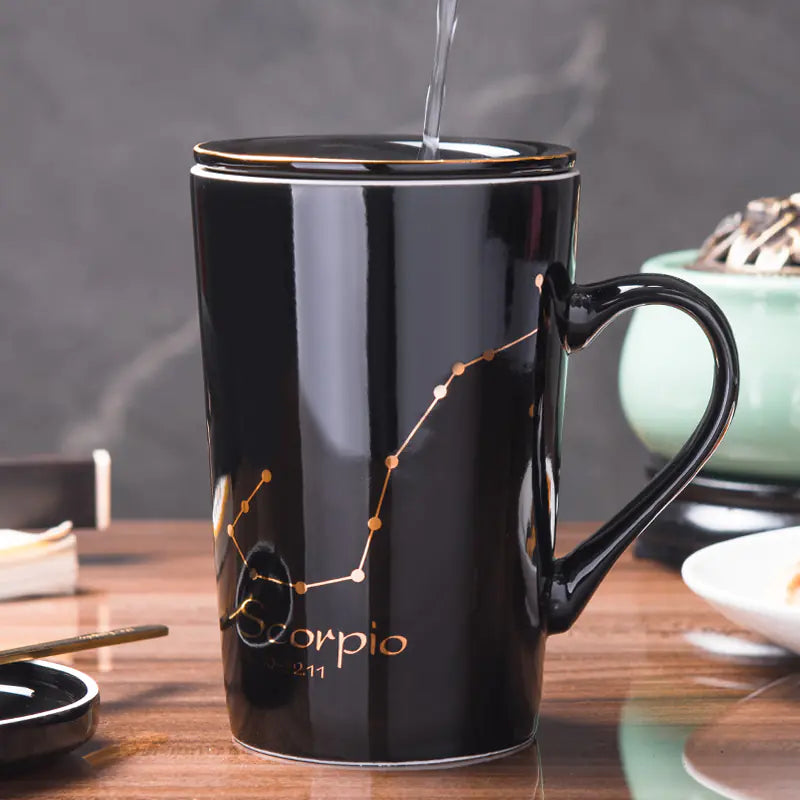 Black mug with Scorpio zodiac design being filled with hot liquid on a wooden table.