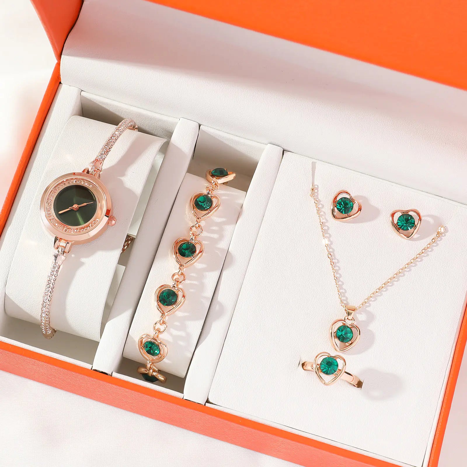 Jewelry set with a watch, necklace, and earrings featuring green gemstones in an open box.