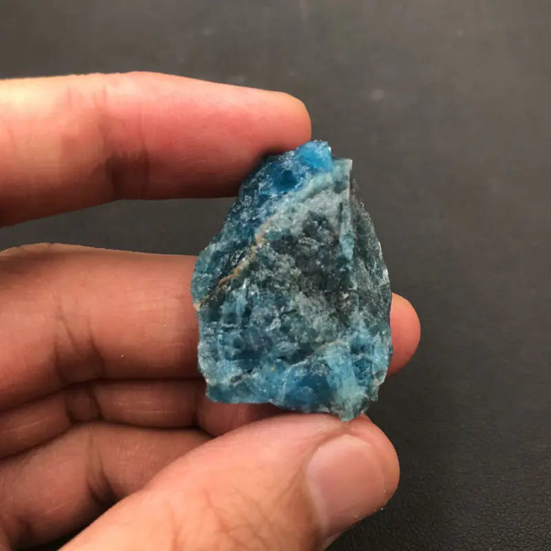 Hand holding a blue crystal against a dark background