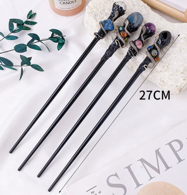 Decorative crystal magic wands with gemstone tips on a white surface with green leaves.