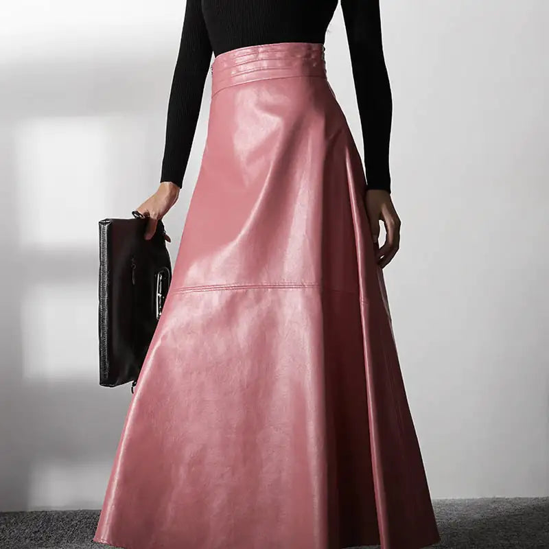 Person wearing a pink leather skirt holding a black clutch against a neutral background