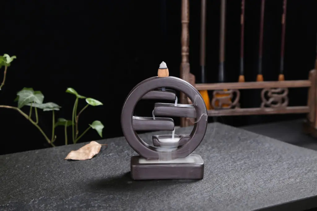 Cylindrical incense burner with a backflow design on a dark surface.