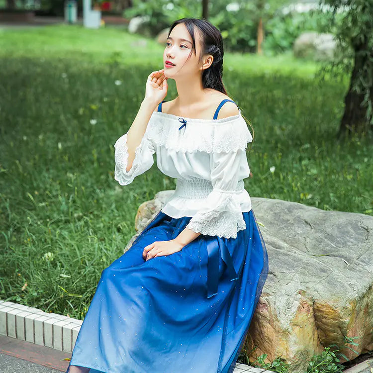 Woman in a white top and blue skirt sitting on a rock in a park.