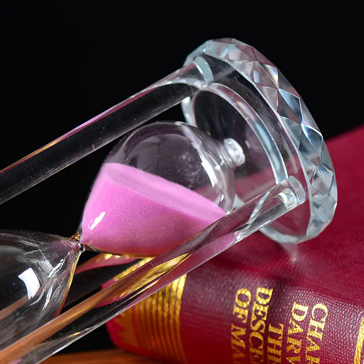 Hourglass with pink sand on a book titled 'The Descent of Man' against a dark background