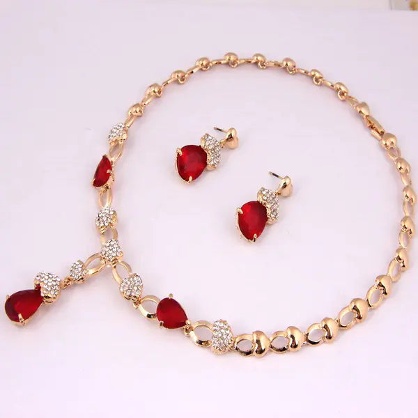 Jewelry set with red stones and gold accents on a light pink background