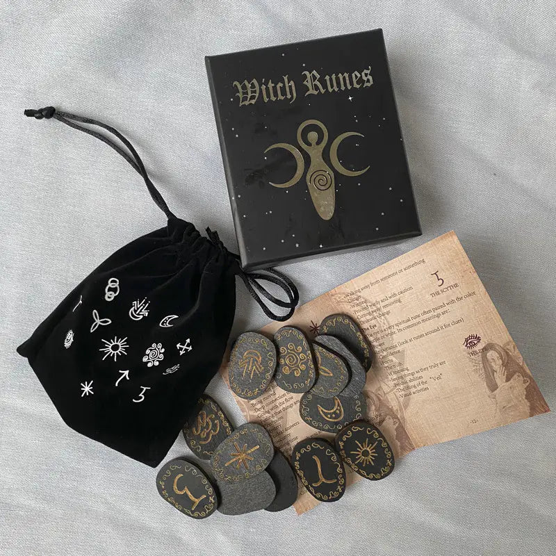 Witch Runes set with black drawstring bag, book, and stones on a gray surface