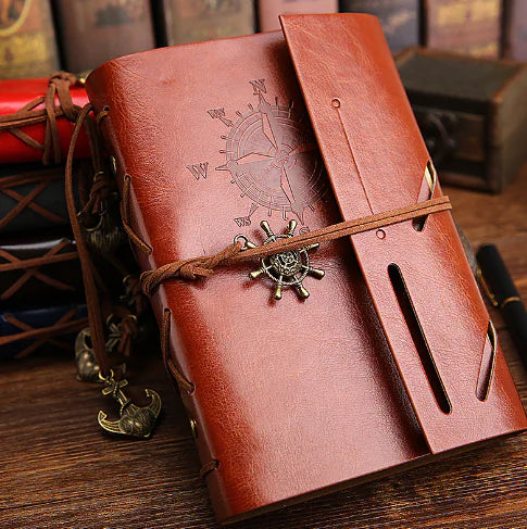 Brown leather notebook with compass design and decorative elements on a wooden surface