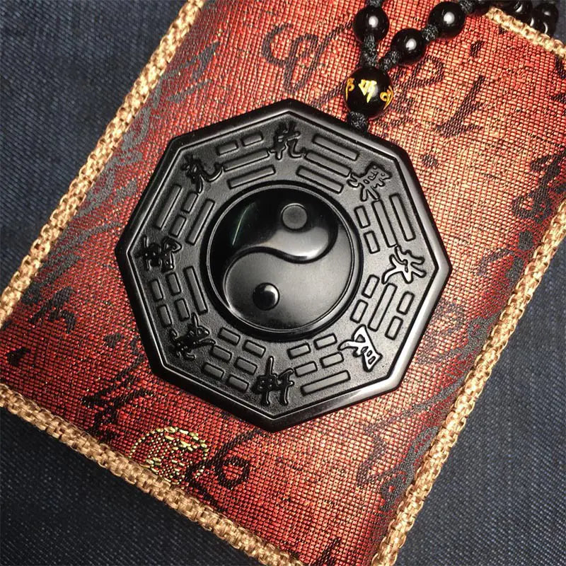 Black hexagonal pendant with yin yang symbol on a red and gold textured background