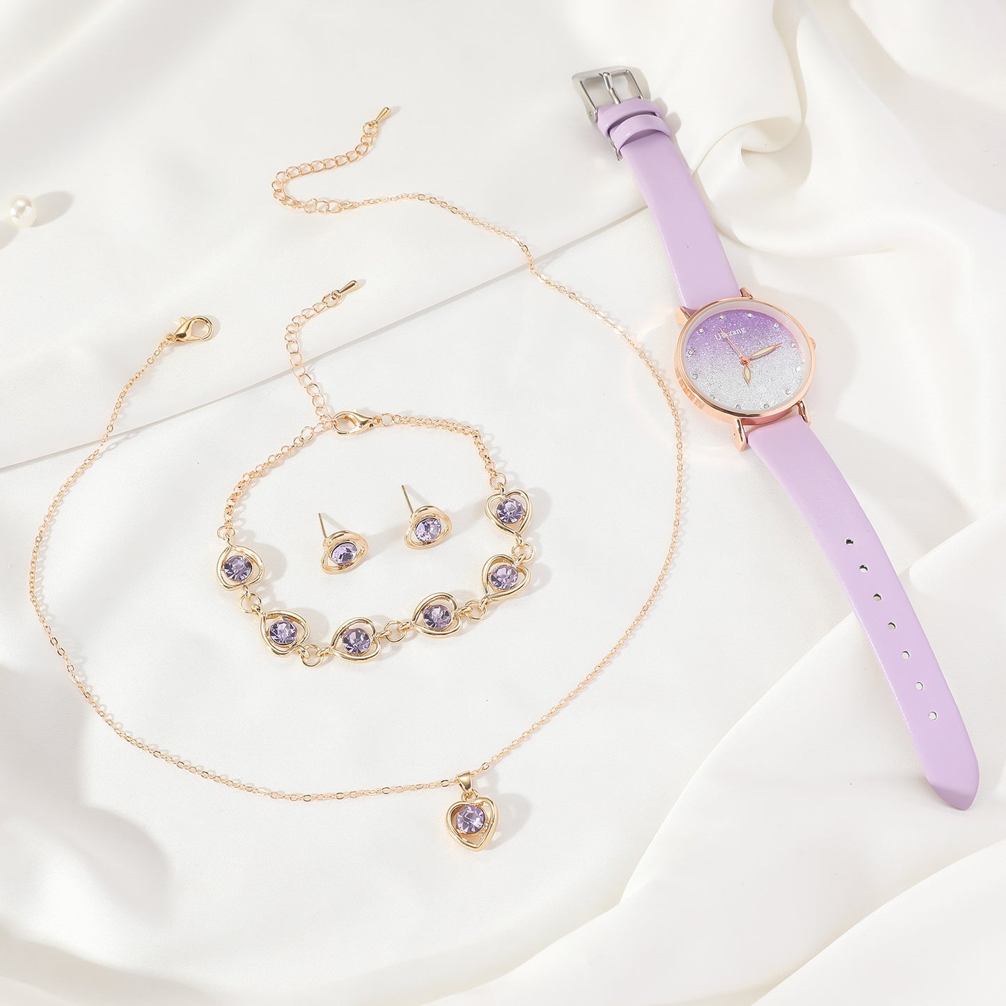 Jewelry set with necklace, bracelet, earrings, and purple watch on a white fabric background