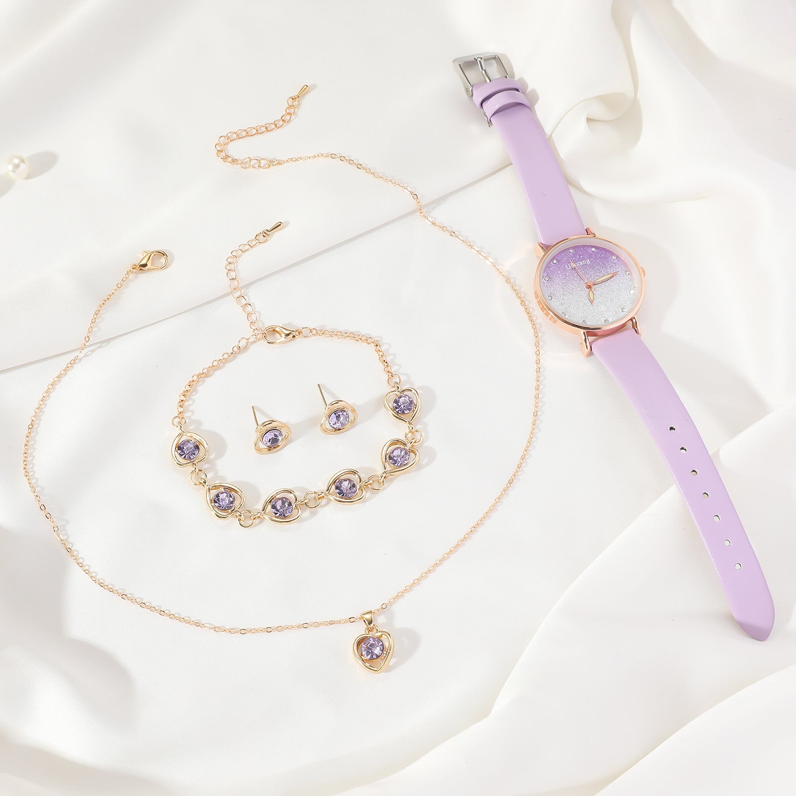 Jewelry set with necklace, bracelet, earrings, and purple watch on a white fabric background