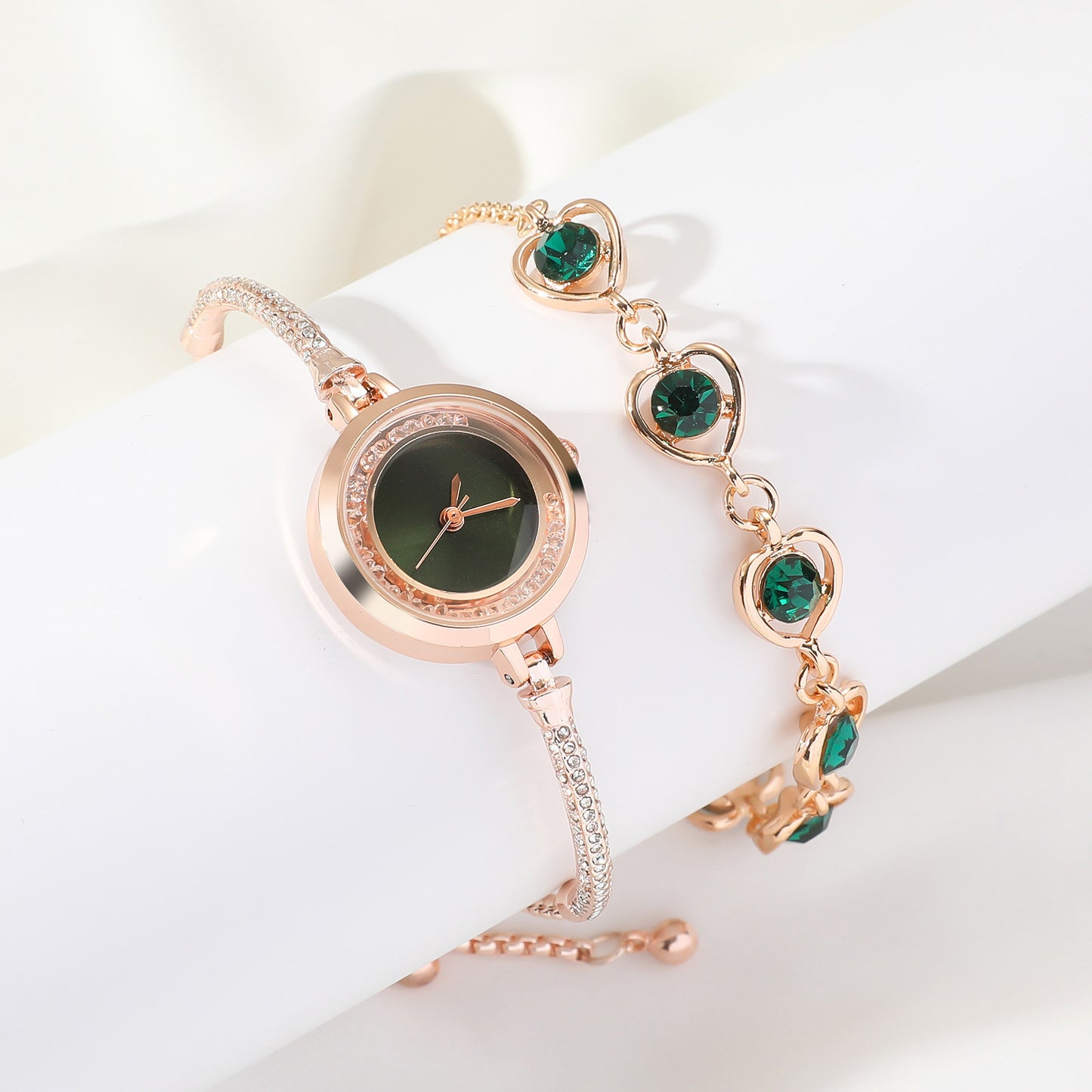 Rose gold watch and bracelet set with green gemstones on a white background