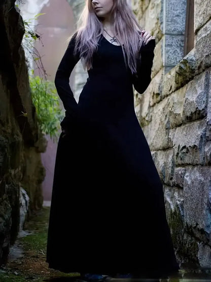 witchy women wearing a long black dress standing against a stone wall.
