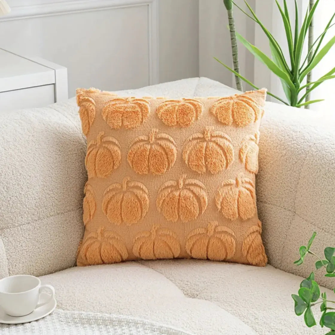 Decorative pillow with pumpkin pattern on a beige sofa with a cup and plant in the background