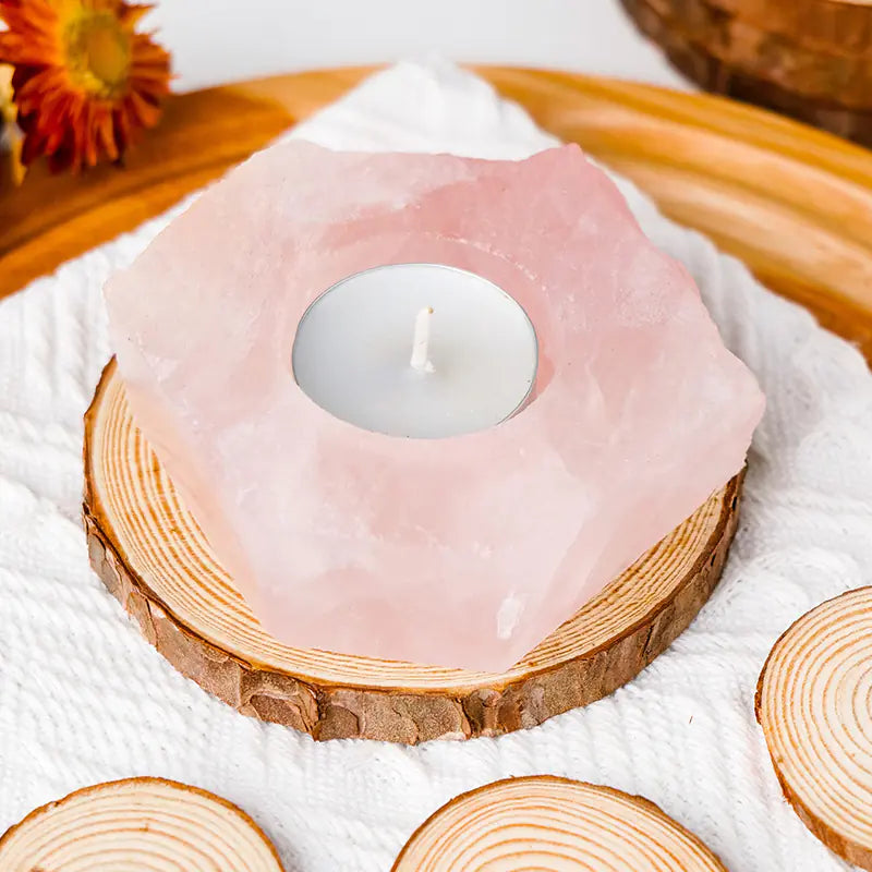 Hexagonal pink candle on a wooden base with a white candle inside, placed on a textured surface.