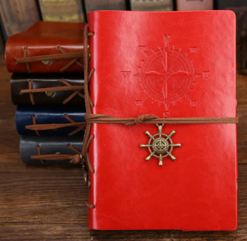 Red leather notebook with compass and ship wheel design on a wooden surface