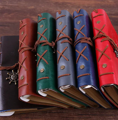 Set of leather-bound books with decorative straps on a wooden surface
