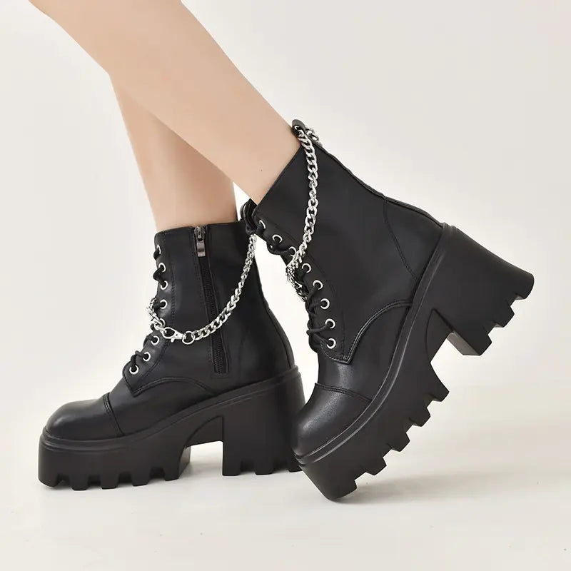 Black platform boots with chain details worn by a person on a light gray background