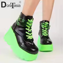 Black platform boots with green soles worn by a person on a white background