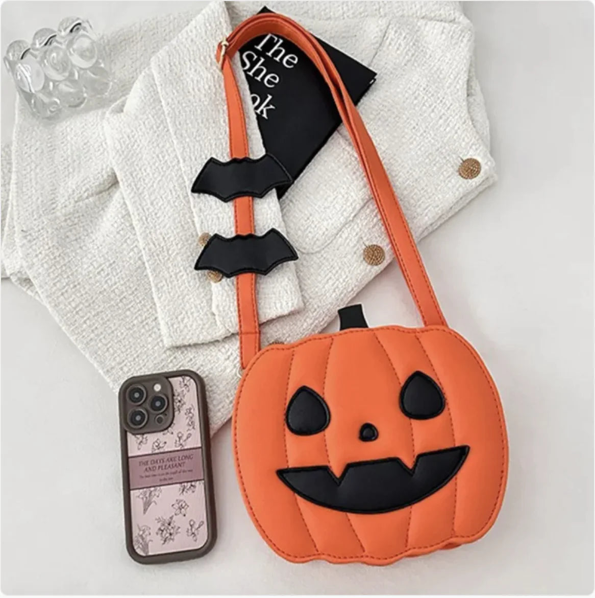 Pumpkin-shaped bag with bat straps on a white surface
