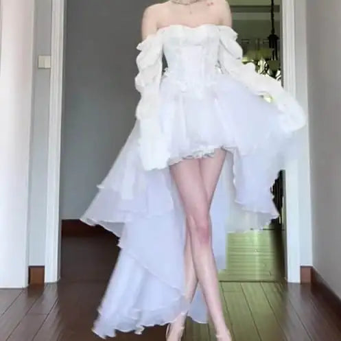 Person wearing a white off-shoulder dress with ruffled layers in a room.