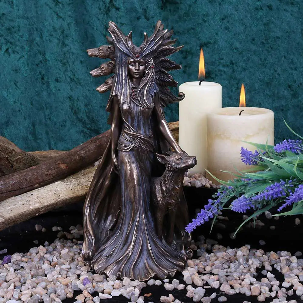 Bronze statue of a hectate with a wolf next to two candles and lavender flowers on pebbles.