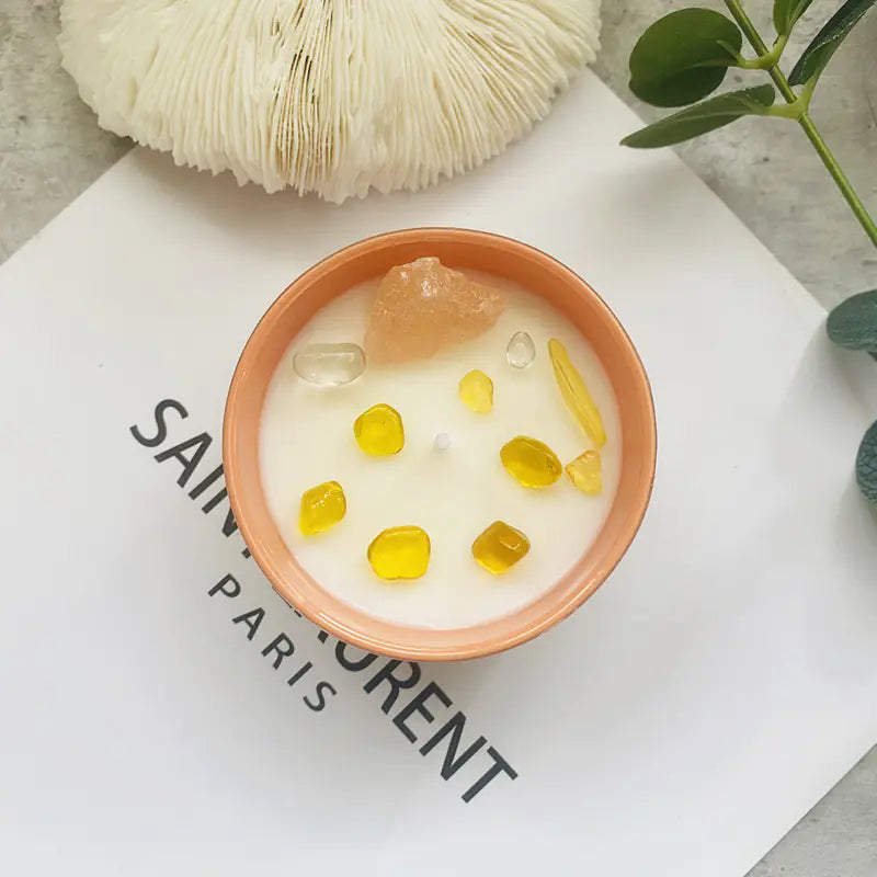 Candle with yellow wax chunks in a terracotta bowl on a white surface with text