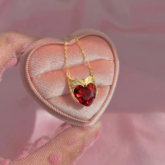 Heart-shaped red gemstone necklace with gold chain on a pink heart-shaped pillow