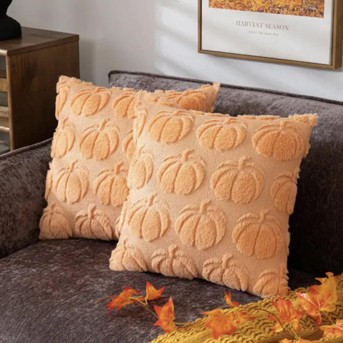 Pumpkin-patterned pillows on a couch with autumn leaves and a 'Harvest Season' sign in the background.