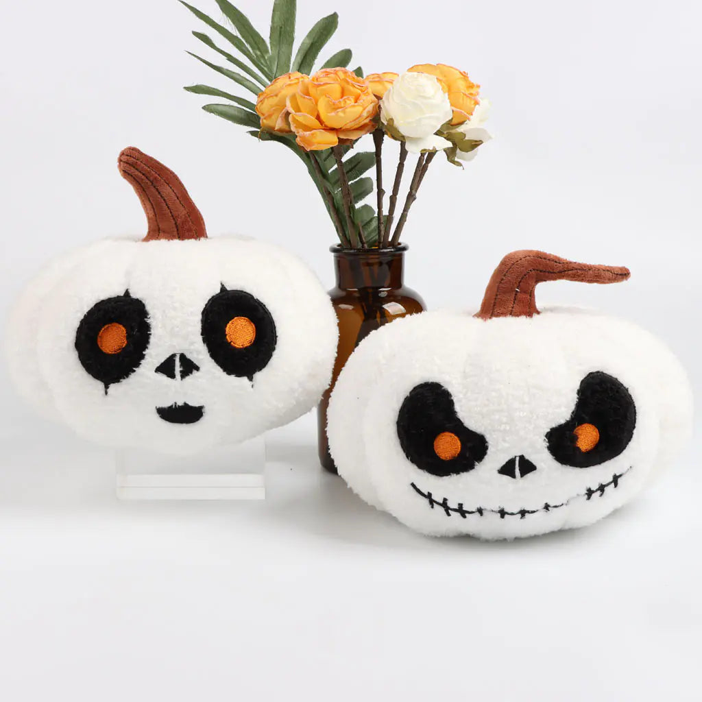 Two white pumpkins with black and orange faces on a white background with a vase of flowers.